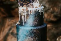 a celestial wedding cake done in navy, with turquoise and golds, with chocolate shards on top and some stars and a moon