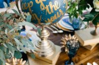 a celestial wedding table with a blue and gold globe, greenery, books, blue glasses and gold cutlery