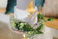 a chic grey and white wedding cake with a marble tier, gold leaf and lots of greenery, blooms and thistles