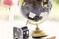 a chic vintage travel-themed wedding centerpiece of a wood slice, a stack of books, a globe and a vintage camera
