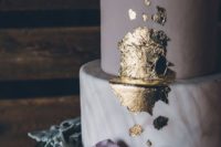 a chic wedding cake with a marble and a purple tier plus gold leaf decor and purple blooms