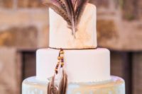 a chic white and blue wedding cake with gold brushstrokes and feathers will fit a boho wedding