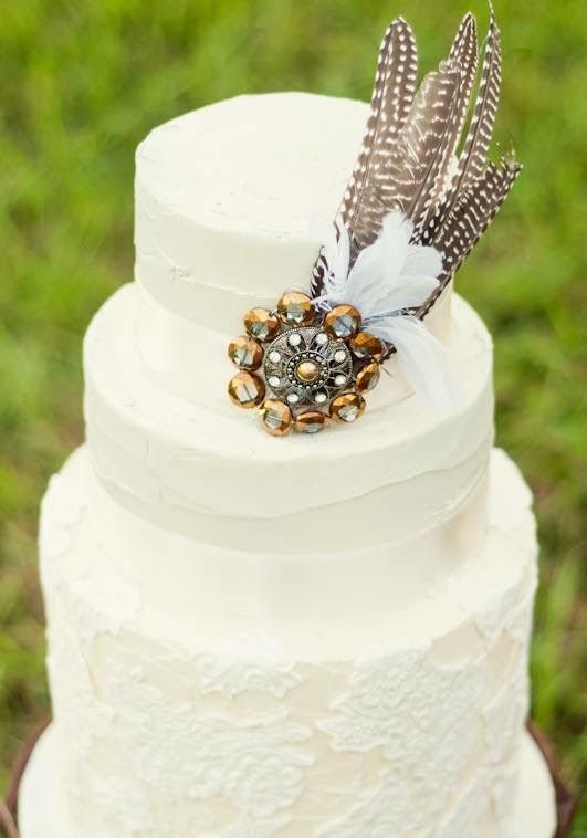 a chic white wedding cake with a lace tier and textural ones, with an oversized embellishments and feathers for a boho wedding