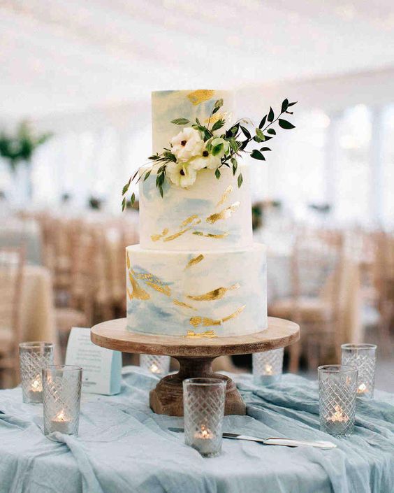 a delicate blue watercolor wedding cake with gold leaf, with white blooms and greenery is a chic idea