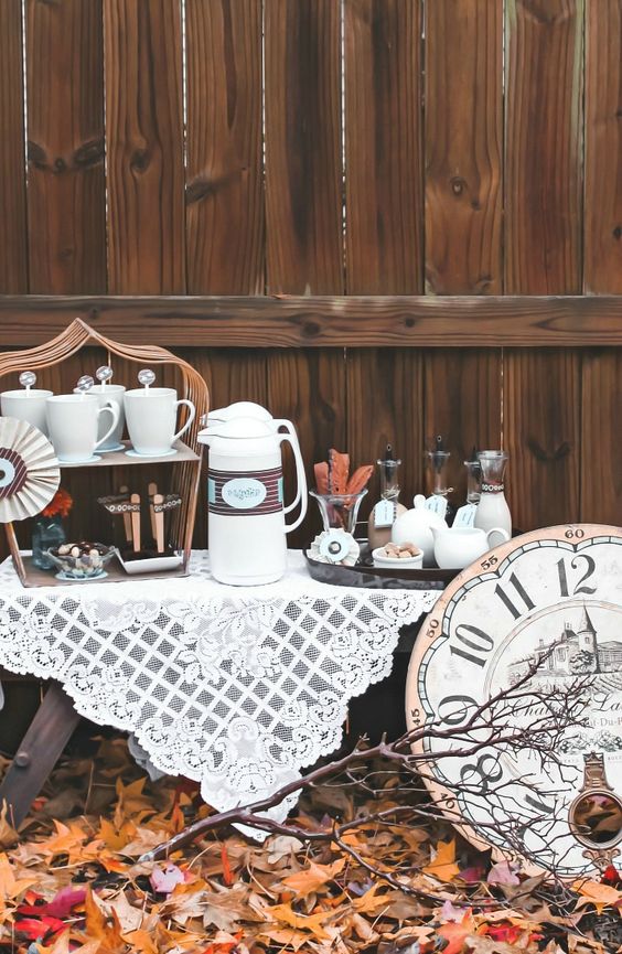 a fall wedding coffee bar with mugs, sweets, tanks and kettles plus a lace tablecloth and a large clock for a vintage wedding