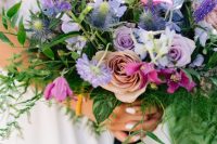 a gorgeous purple wedding bouquet with lilac roses, thistles, purple freesias, lisianthus and greenery cascading