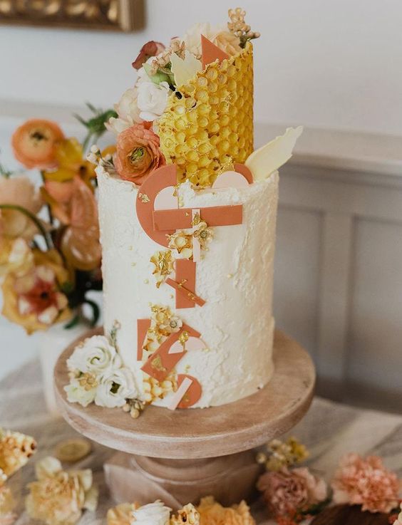 a gorgeous white wedding cake with sugar letters, topped with honeycombs, blooms and gold touches is amazing for a honey-themed wedding