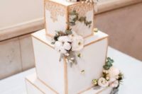 a luxurious white wedding cake with gold framing, fresh blooms and greenery