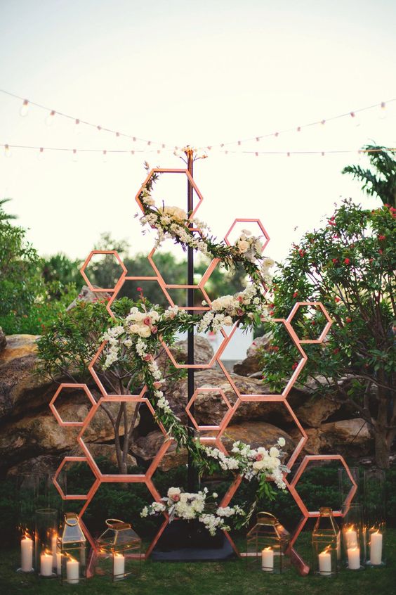 a modern rustic wedding backdrop of wooden honeycombs with blooms and greenery, pillar candles and candle lanterns