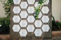 a modern rustic wedding seating chart of a large timber piece, honeycomb seating chart, greenery and white blooms
