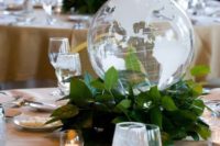 a modern wedding centerpiece of a greenery wreath and a sheer globe is a stylish idea for a travel-themed wedding