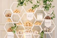 a modern white honeycomb stand with lots of glazed donuts and greenery is a ccreative alternative to a usual wedding dessert table
