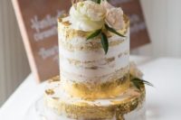 a naked wedding cake with gold leaf, neutral and pastel blooms and a gold cake topper