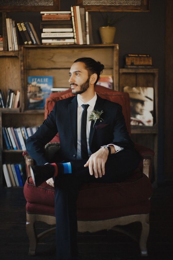 a navy suit, a black tie, a greenery boutonniere, striped socks for an accent and a man bun for a mid-century modern look