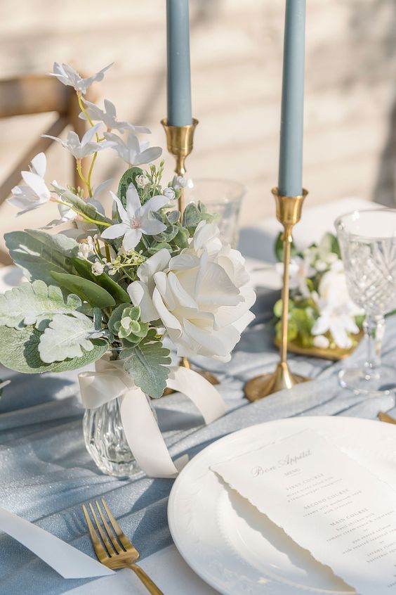 a neutral and delicate wedding centerpiece of greenery and pale leaves, a white rose and freesias plus a bow is amazing