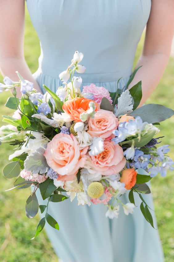 a pretty wedding bouquet of pink roses, coral ranunculus, blue delphinium, greenery and pale foliage is a chic idea