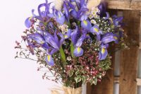 a pretty wedding bouquet with blue irises, chamomiles, greenery and some colorful fillers is idea for a countryside or boho bride