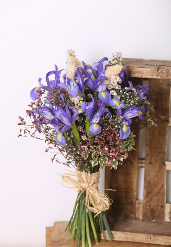a pretty wedding bouquet with blue irises, chamomiles, greenery and some colorful fillers is idea for a countryside or boho bride