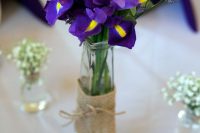 a pretty wedding centerpiece of lavender and irises plus foliage in a tall bottle wrapped with burlap is a lovely idea for a spring or summer wedding