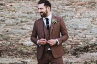 a refined groom’s look with a three-piece rust tweed suit, a white button down, a blakc tie and brown shoes
