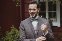 a relaxed groom’s outfit with a brown tweed blazer, grey pants, a grey waistcoat, a white button down and a green bow tie