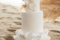 a romantic white wedding cake with sleek and ruffle tiers, with gold tipped feathers