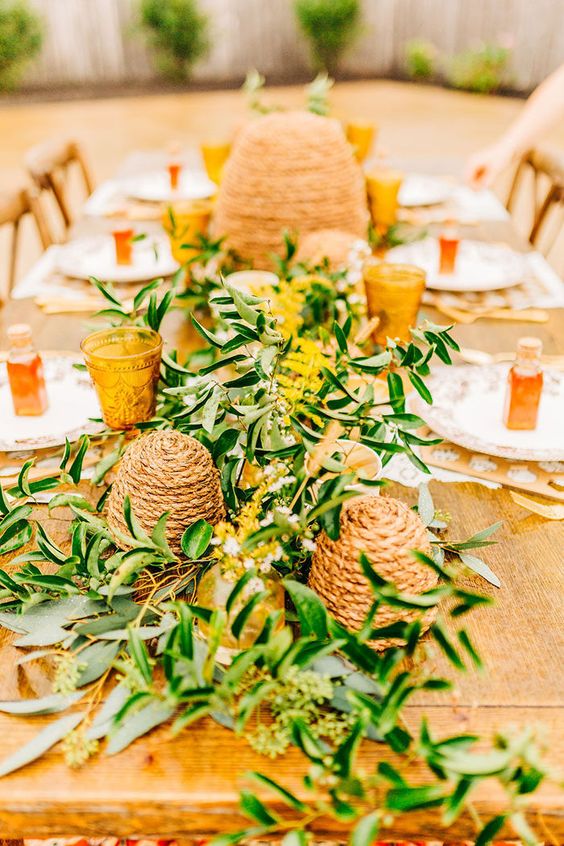 a rustic boho wedding tablescape with a lush greenery and mimosa runner, hives made of jute rope and amber glasses