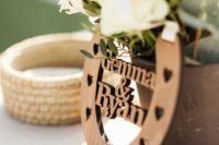 a rustic wedding centerpiece of a vase, white blooms and greenery and a plywood horseshoe with names