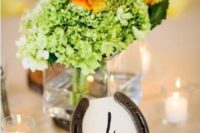 a rustic wedding centerpiece of green hydrangeads and bold leaves, candles and a horseshoe table number