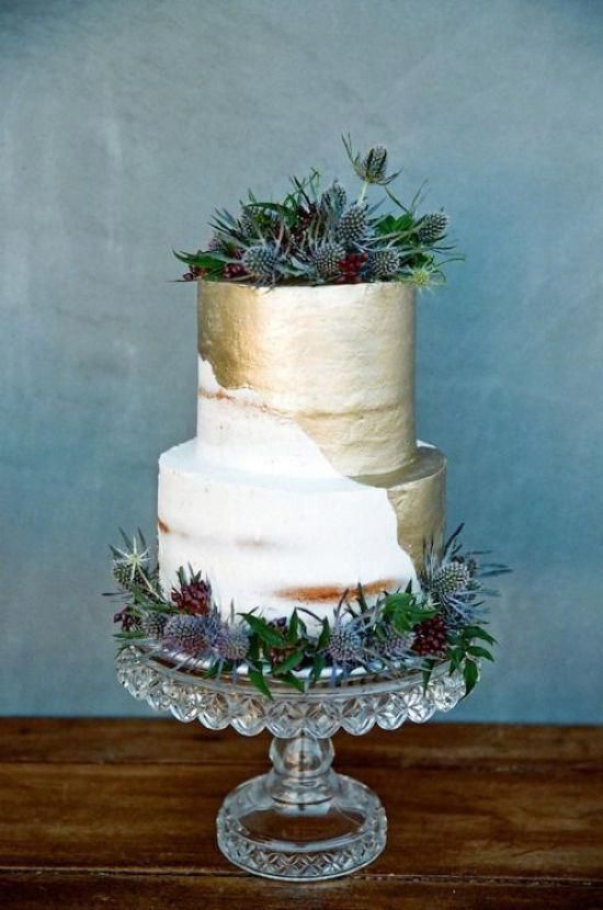 a semi naked wedding cake with much gold leaf, berries and thistles looks bold and catchy