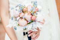 a small and cute wedding bouquet of blush peonies, serenity blue blooms, lace and navy ribbons for a contrast