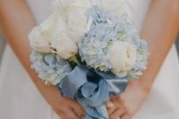 a small and delicate wedding bouquet of white roses and blue hydrangeas with a matching blue ribbon bow