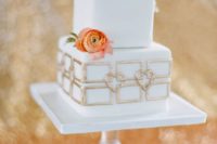 a square wedding cake with gold decor and fresh blooms and an air plant on top for an elegant wedding