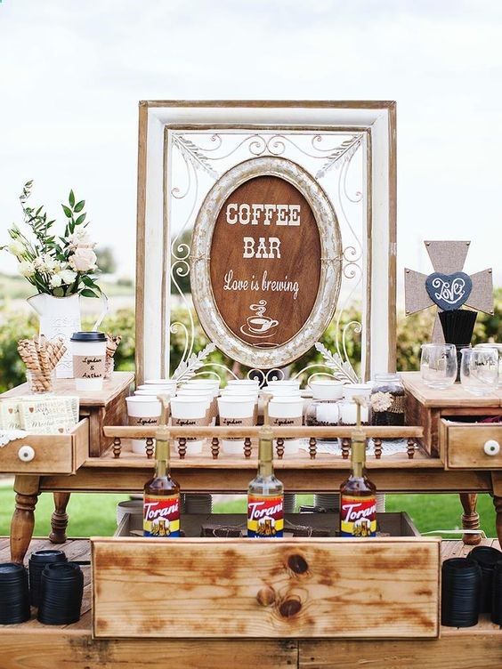 a stylish coffee bar with a large vintage sign, coffee cups, liquors and various sweets and blooms for decor