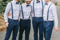 a stylish groom’s outfit with navy pants and suspenders, light blue shirts, navy bow ties, brown shoes