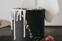 a textural black wedding cake with white dripping, gold leaf, painted and fresh blooms and white chocolate shards