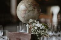 a travel wedding centerpiece of a globe, a suitcase, a neutral bloom and greenery arrangement