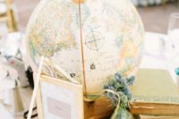 a travel wedding centerpiece of stacked books, a sign, thistles in a bottle and a large globe