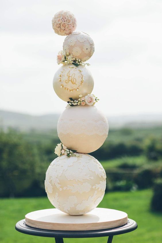a very whimsical sphere wedding cake in white and tan, with floral and lace patterns, with pink blooms and greenery