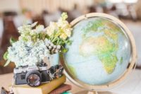 a wedding centerpiece of a stack of vintage books, a vintage camera, pastel blooms and a large globe for a travel-themed wedding