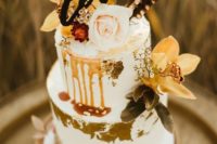 a white fall boho wedding cake with gold leaf, moody blooms and foliage, blush rose and feathers on top