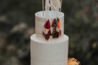 a white textural wedding cake with bright feathers and a macrame topper plus bold blooms for a fall boho wedding