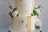 a white wedding cake with gold leaf, caramel drip, white blooms, greenery and green macarons