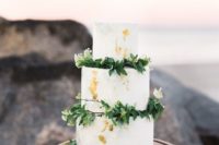 a white wedding cake with gold leaf, greenery and white blooms is a universal cake for any season