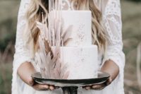 a white wedding cake with silver leaf and blush sugar feathers and thin and tall candles in blush