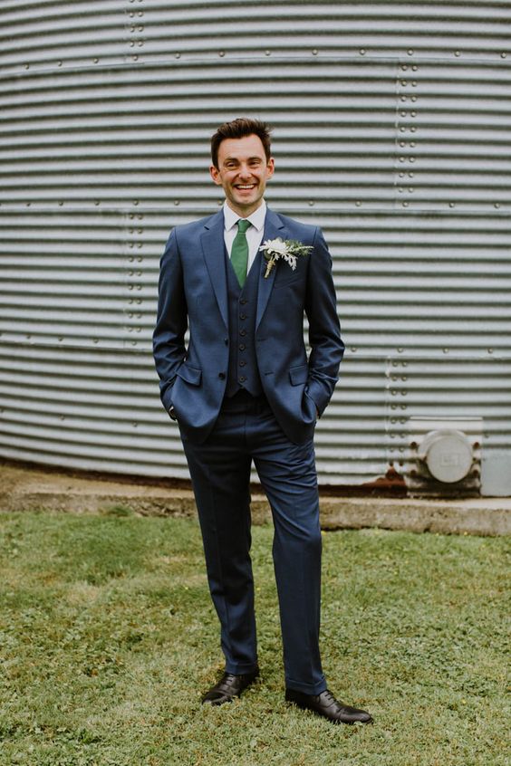 an elegant groom's outfit with a thre-epiece navy suit, an emerald tie, a white button down and black shoes