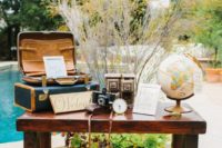 travel-themed wedding decor – suitcases, a globe, vintage cameras and greenery and branches behind the table