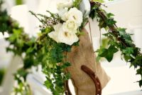 wedding aisle chairs accented with greenery, white blooms and horseshoes for a cozy rustic feel
