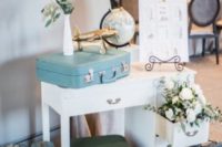 wedding decor done with lots fo vintage suitcases, white blooms and greenery, a globe and a plane