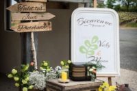 wedding decor of vintage suitcases, bright yellow blooms, a sign, candle lanterns and a sign with wooden elements